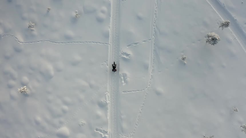 Overhead drone aerial of a bicycle riding through the snow