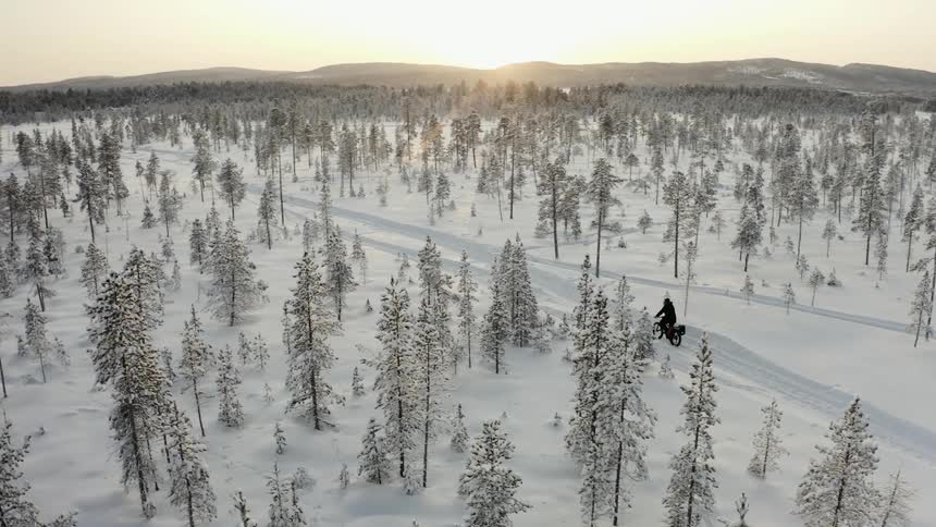 Man rides a bicycle on snowy forest track at sunset