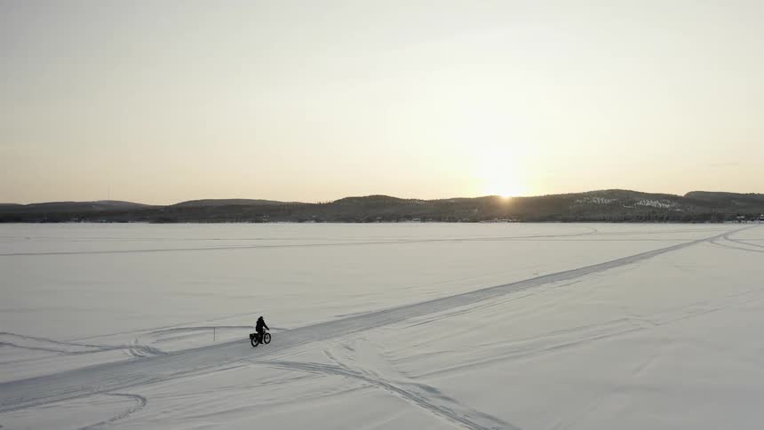 Man rides bicycle on road through snow covered plain