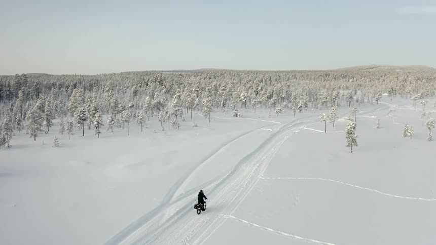 A person fatbiking on a snow covered path towards trees