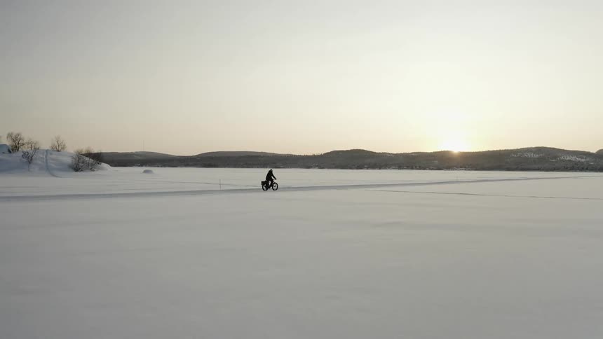 A person rides a bicycle through a field on a snow covered trail