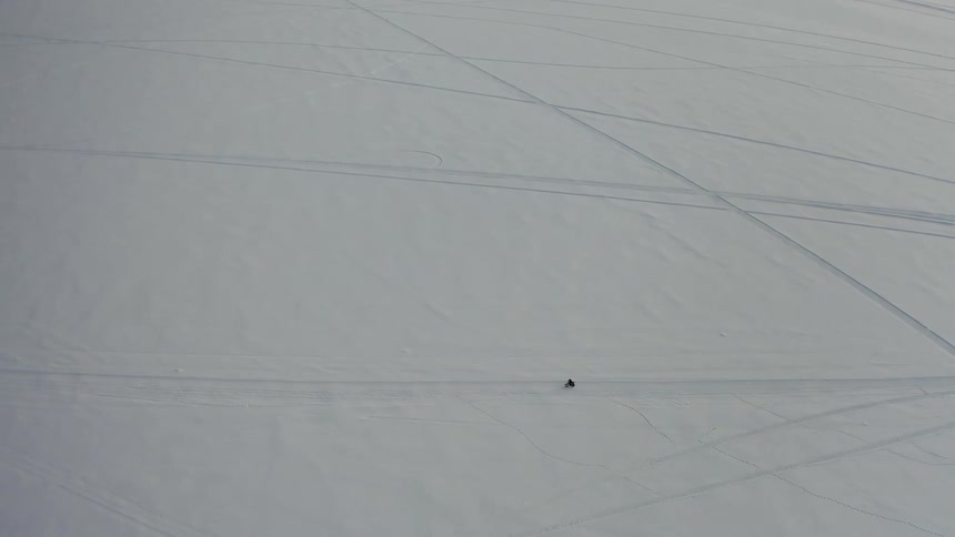 A solitary person rides a bicycle across a barren and expansive snow covered landscape