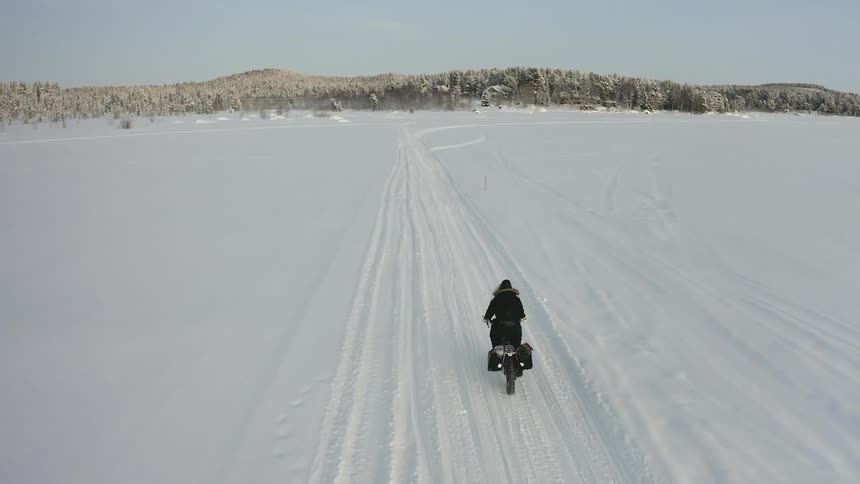 A person rides a bike down a snow covered road