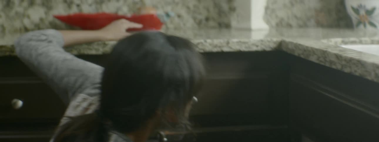 An indian woman pulls her head out of a cabinet in a kitchen and stands up