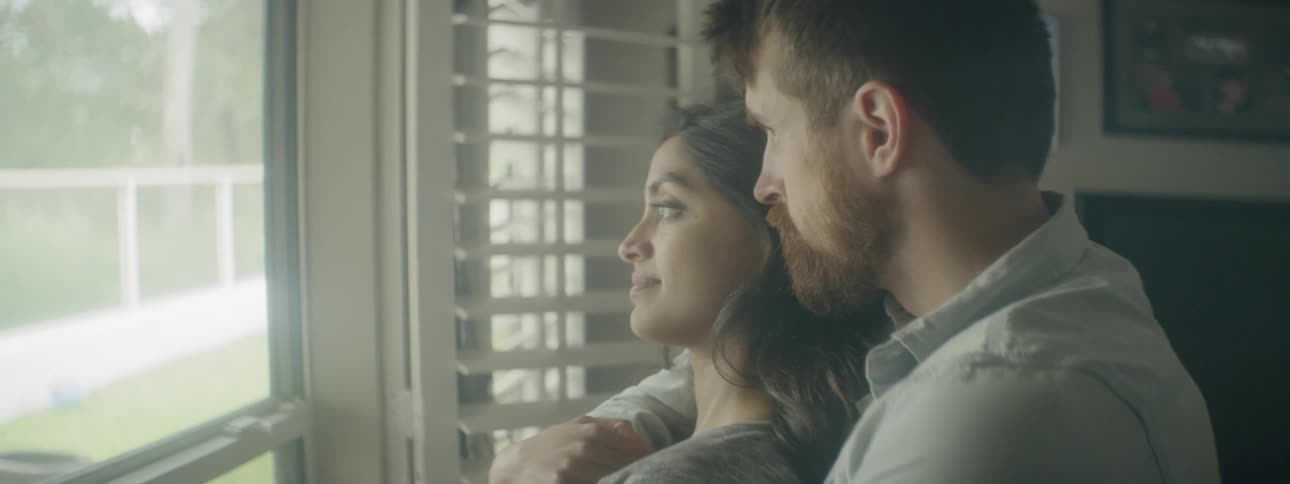 A man and a woman embrace while looking out of a window