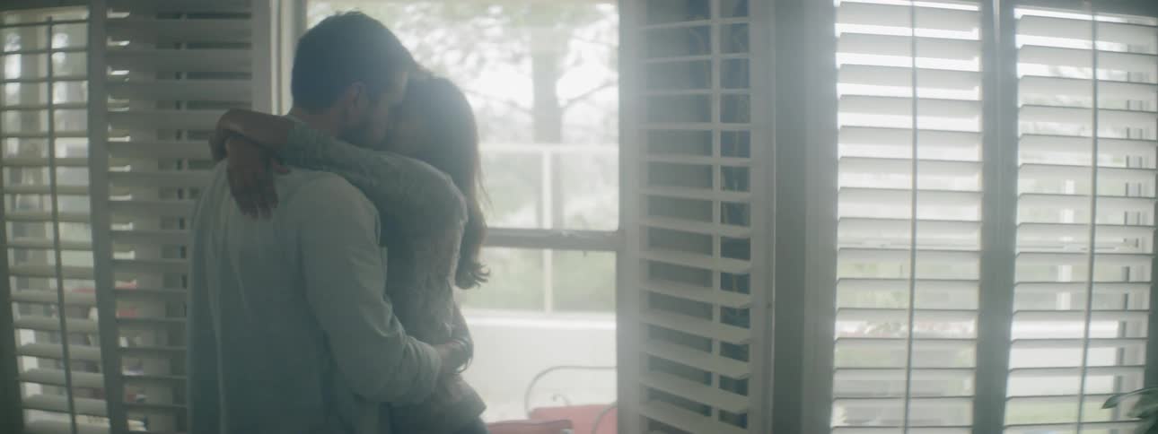 Man and woman cuddle and kiss each other in front of the terrace door in the house
