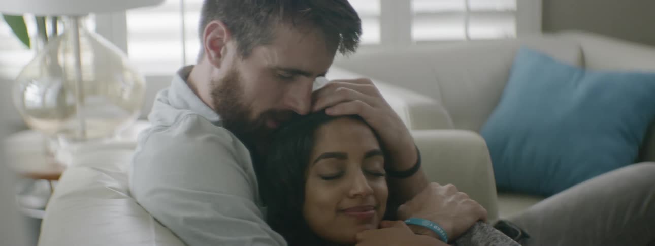 A woman smiles as her man hugs her and cuddles with her on the couch