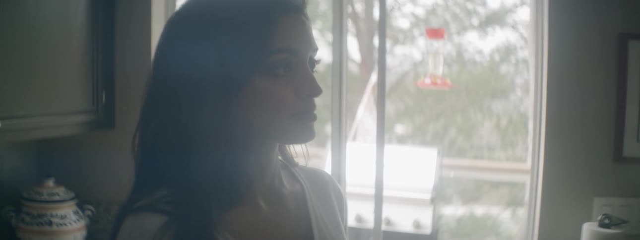 A woman stands indoors in a kitchen area while talking to someone