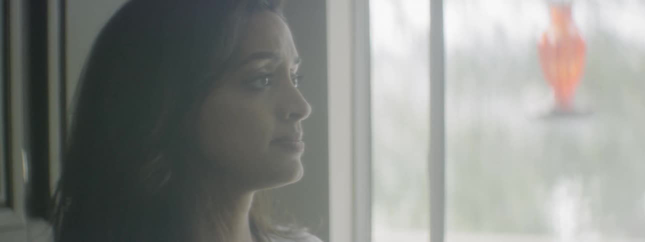 A woman talks while looking out a window and appears concerned and sad