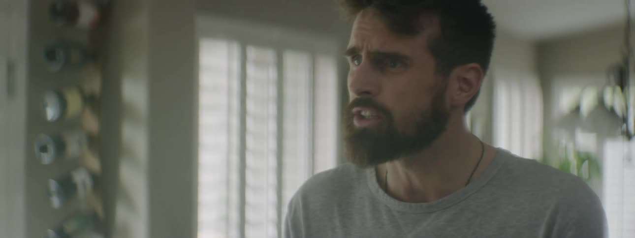 A bearded man with a look of frustration on his face is speaking emphatically to another person