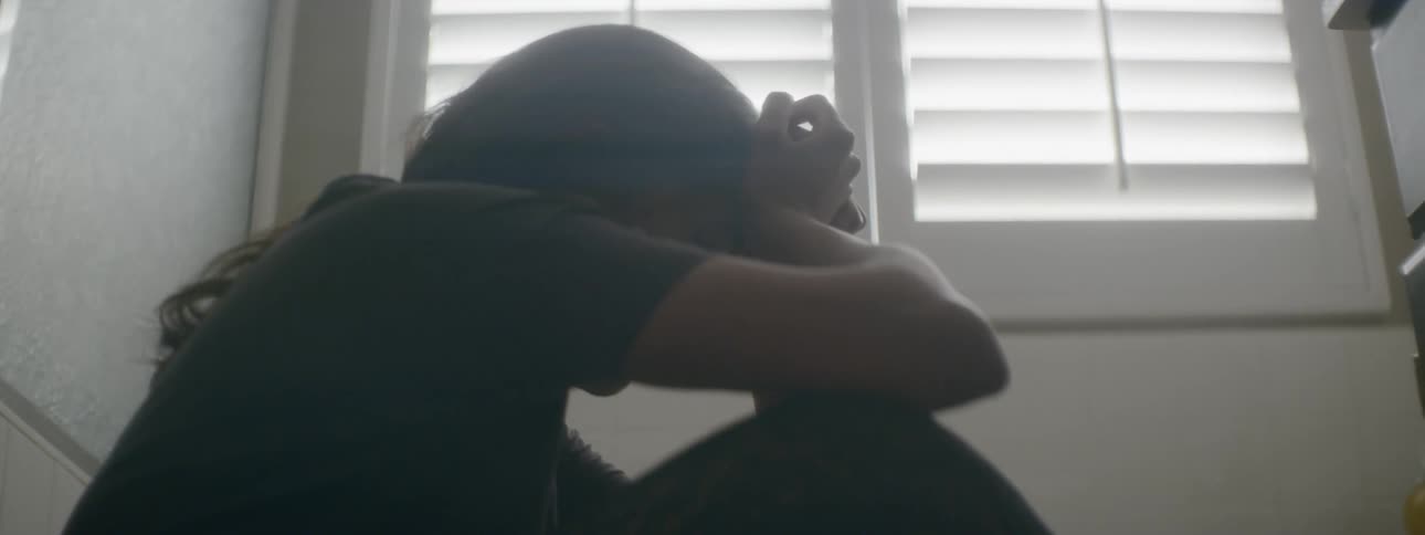 Woman sitting in stairwell holding head in hands under window