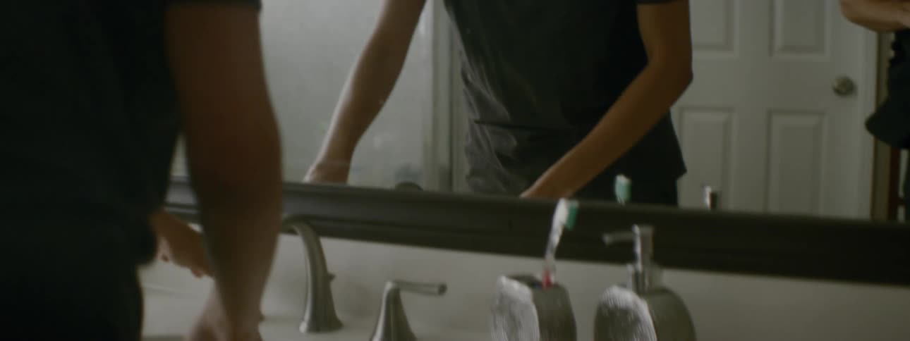 A woman washes her face in a bathroom sink