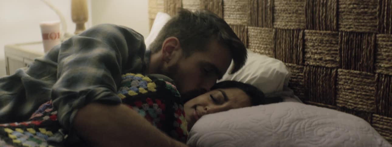 Man lying down on the bed spoons woman in the bedroom