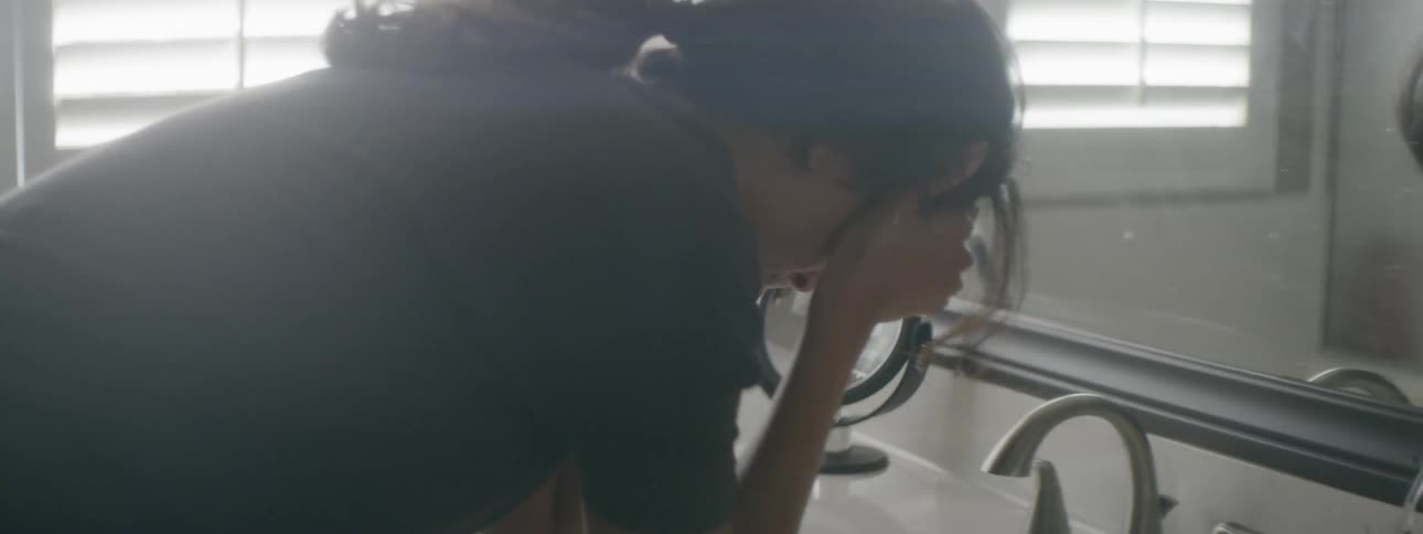 A woman leans over a bathroom sink with her head in her hands