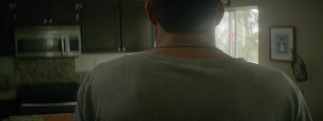 A man walks through a house and into the kitchen where a woman is washing a pan in the sink