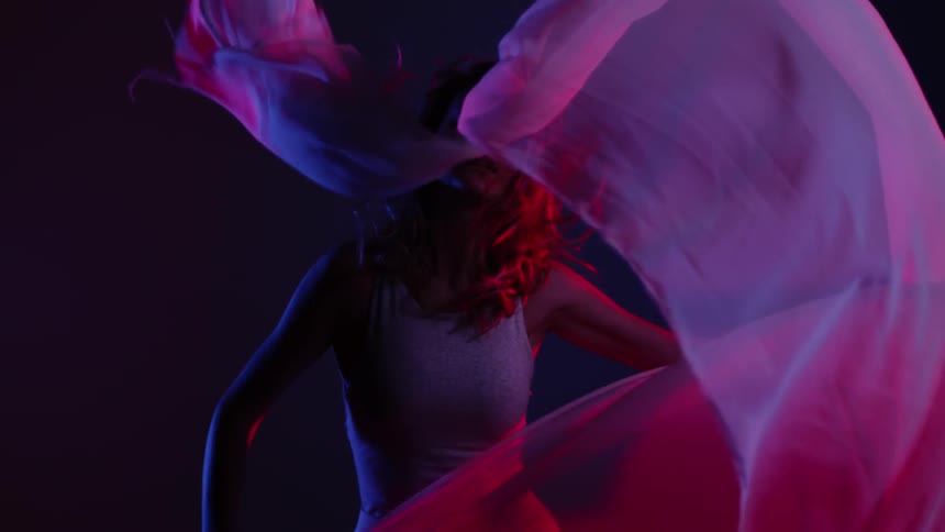 A woman stands in the dark and waves around a filmy sheet