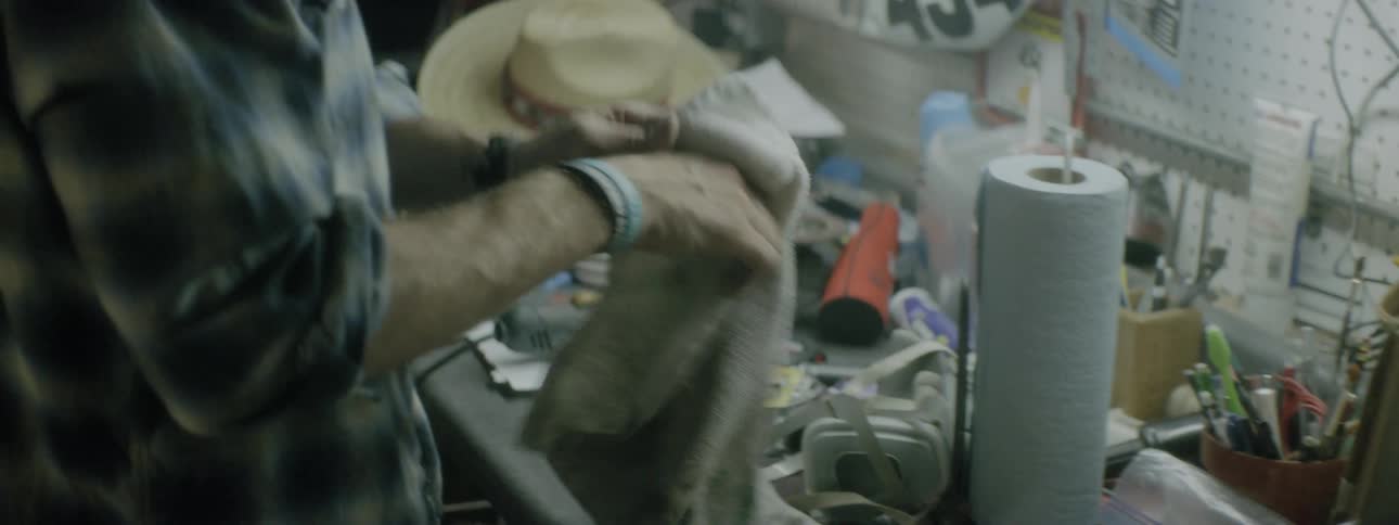 A man standing by a workbench wiping his hands with a rag