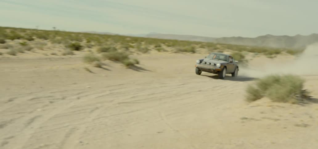 A sports car races along a dirt path in the middle of a desert landscape