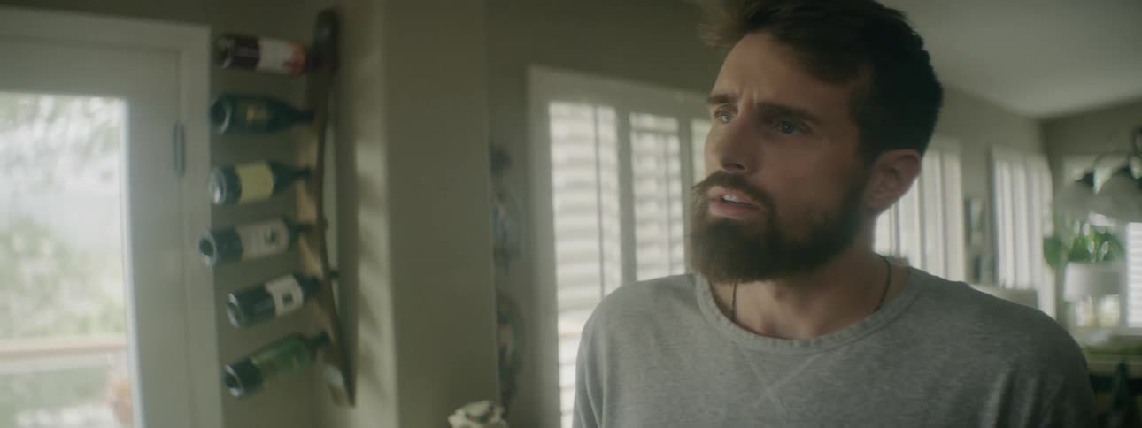Bearded man stands inside home talking to someone