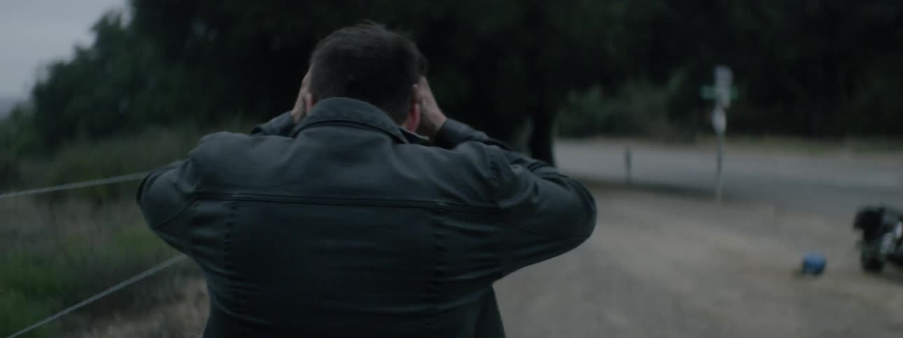 A bearded white man walks across a rest area on the side of a road