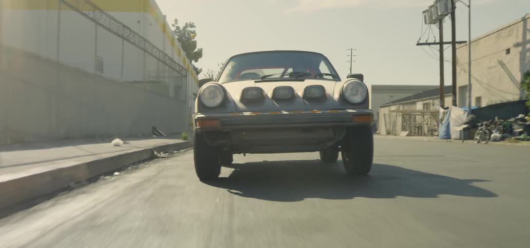 Man drives sports car rapidly along road past buildings