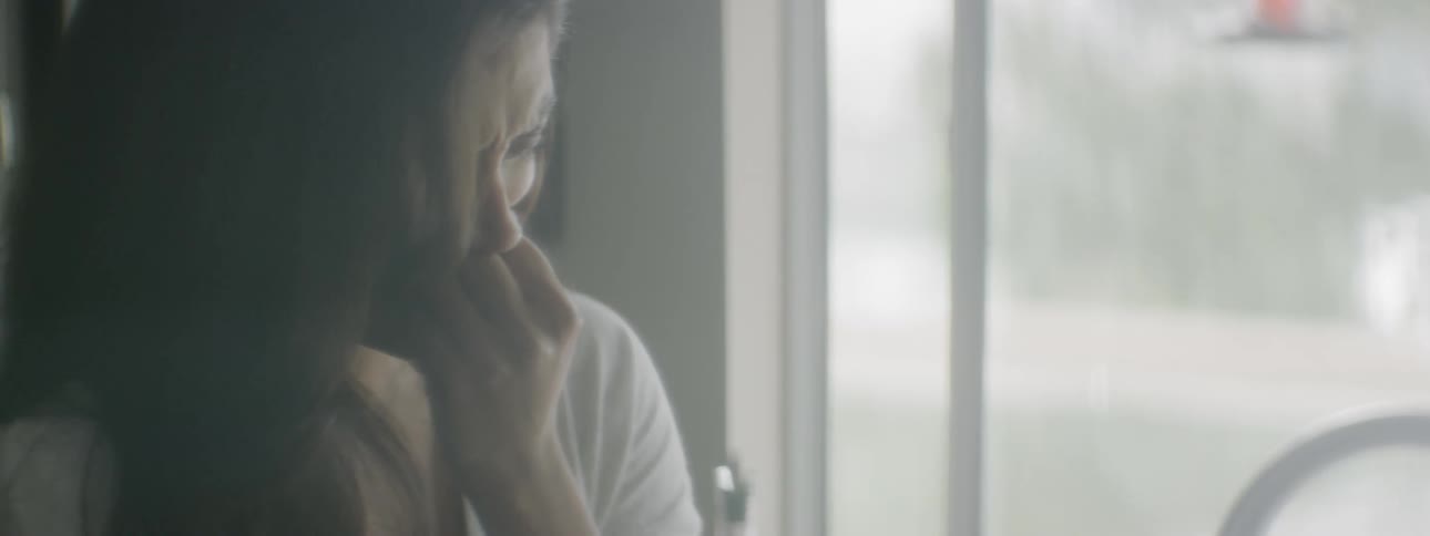 A woman standing by a window crying