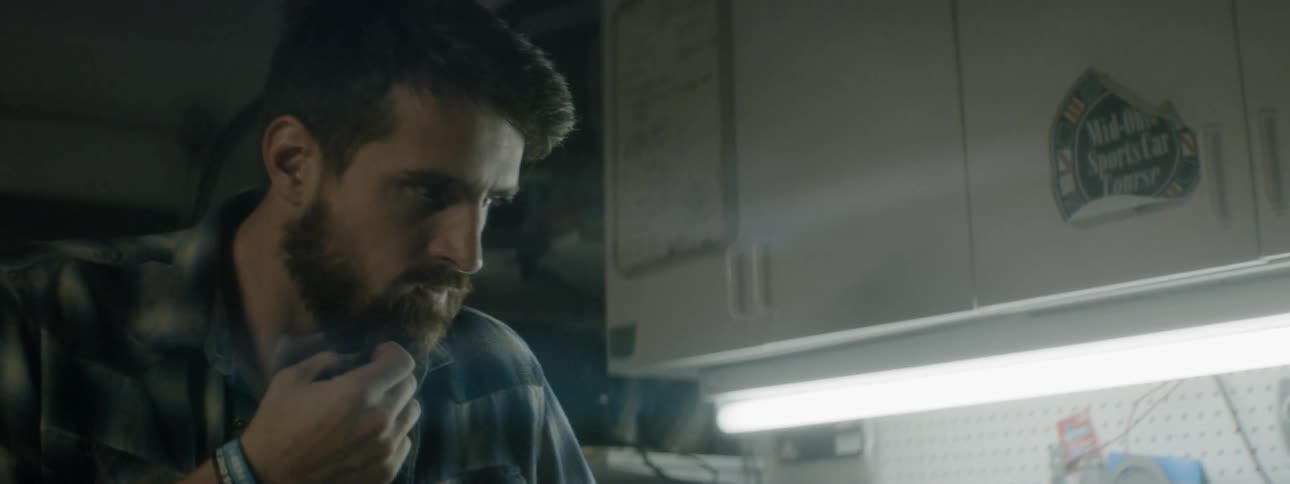 A man stands by a workshop bench thinking with his hand on his chin