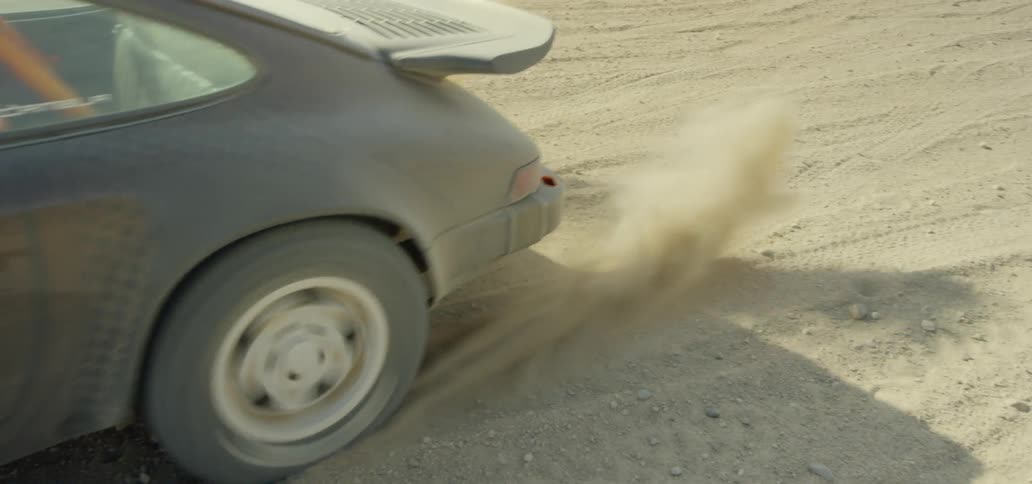 A sports car on a dirt surface quickly accelerates and kicks up a ton of dust