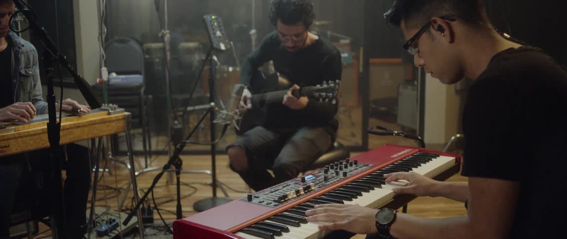 A group of men sit in a room together and play musical instruments