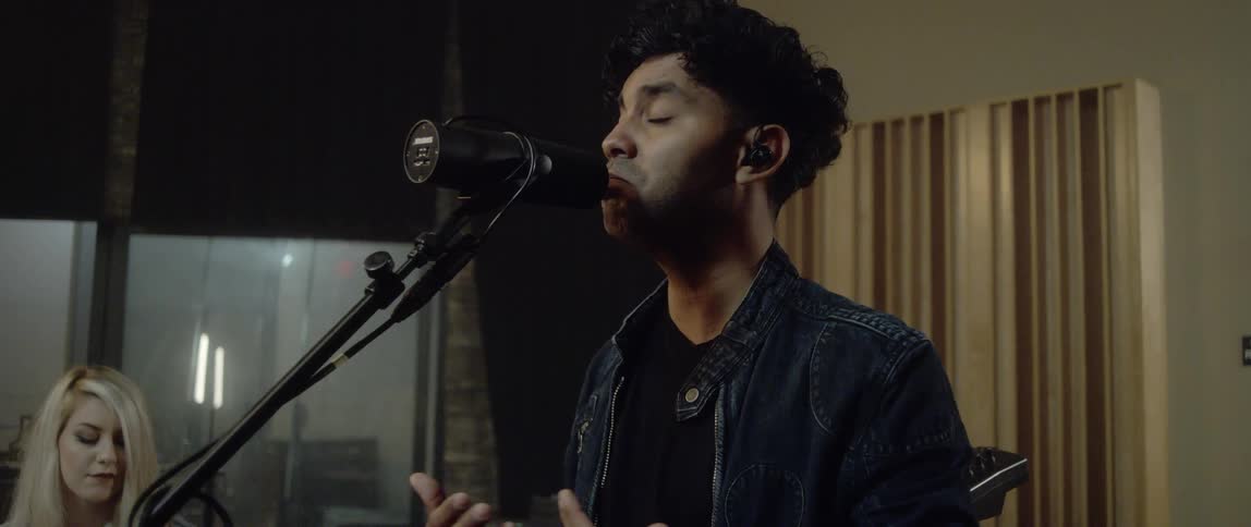 An indian man sings into a microphone in a recording studio