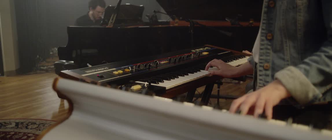 A musician plays two keyboards at once while another plays the piano