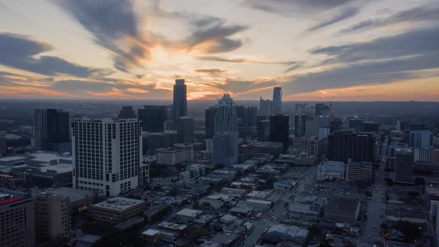 The sun sets on the horizon over skyscrapers as traffic moves on city streets