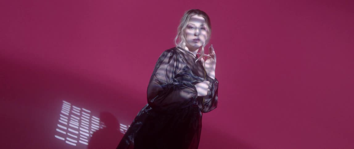 A woman standing in a pink room with lights on her face