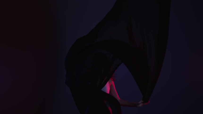 A woman dances with a black cloth in a dark room