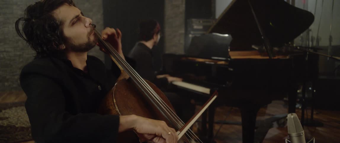 Musicians play string instruments and the piano in a band