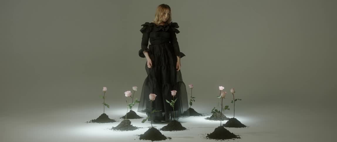 A woman in black stands near many pink roses stand upright in dirt