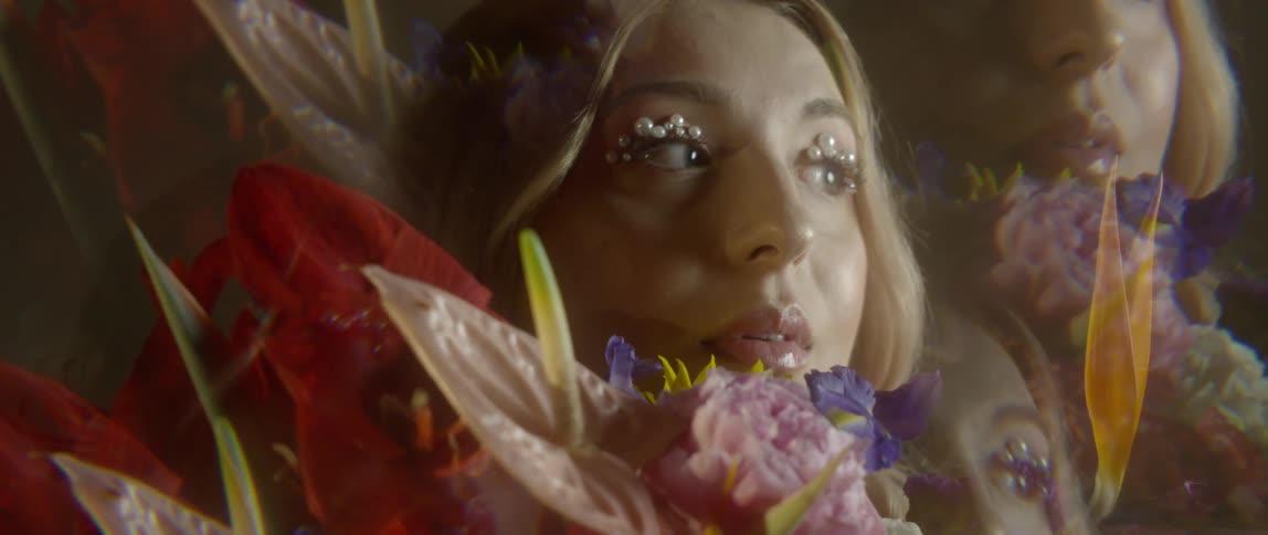 A blonde woman with pearls on her eyelids holds a bundle of flowers