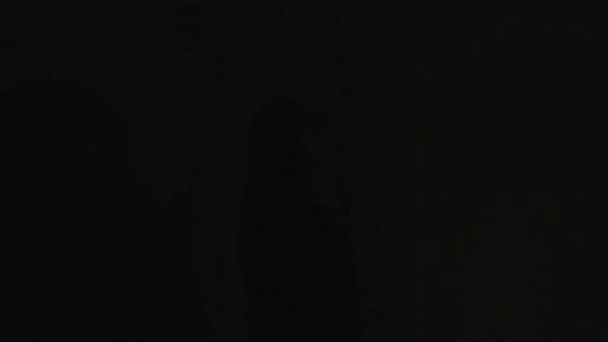 Lights flash briefly to see a woman standing in front of a red curtain
