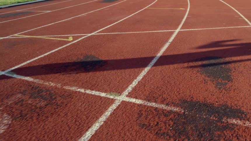 A runner's shadow is cast on a racing track