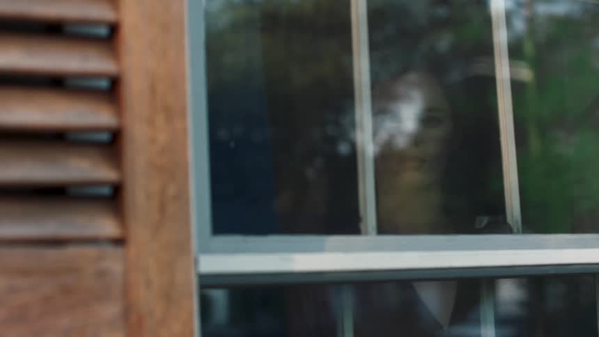 A woman standing and looking out a window then walking away