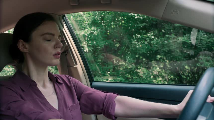 A woman sits in the drivers seat of her vehicle and closes her eyes