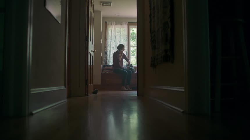 A woman quickly puts items into her purse while sitting in her house and talking on the phone