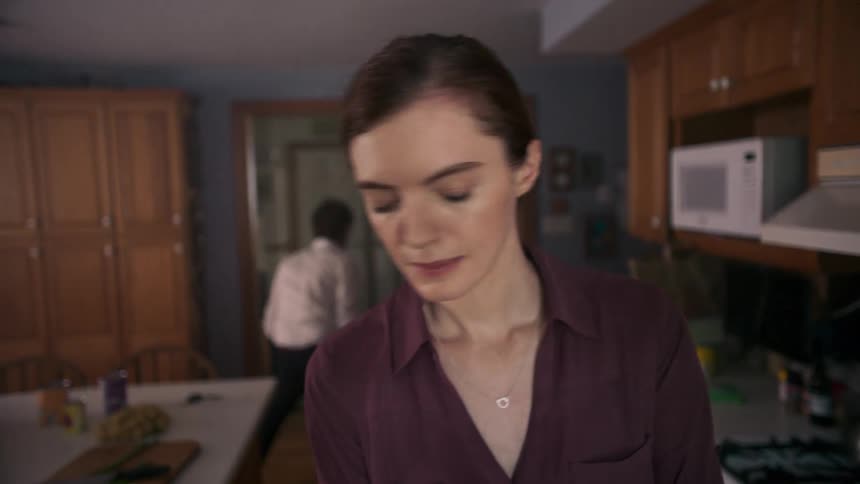 A woman preparing food in the kitchen while a man plays with a little girl in the background