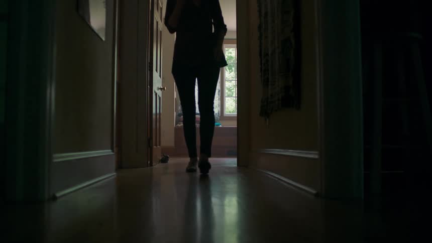 A woman walks down the hallway of her house while looking at her phone