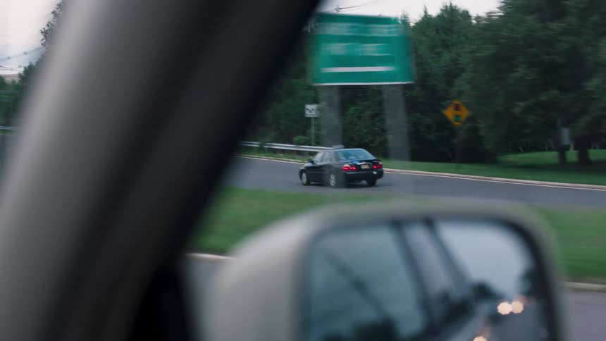 A taking a highway exit is visible through the passenger side window of a car traveling on a multi lane highway