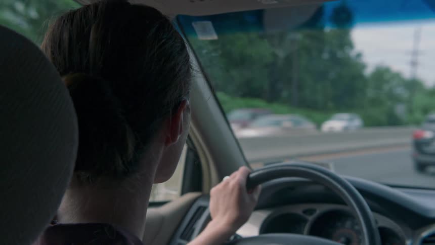 A woman holds the steering wheel with one hand as she drives on a multi lane highway