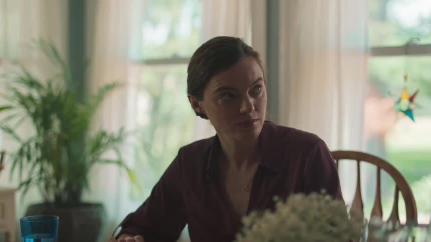A woman chewing food while listening to someone while sitting at a dinner table
