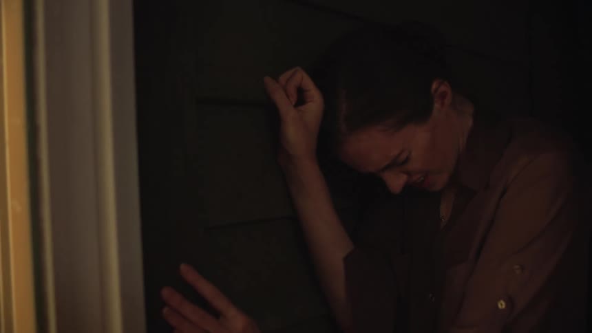 Woman leaning against the door keeps her head down in agony