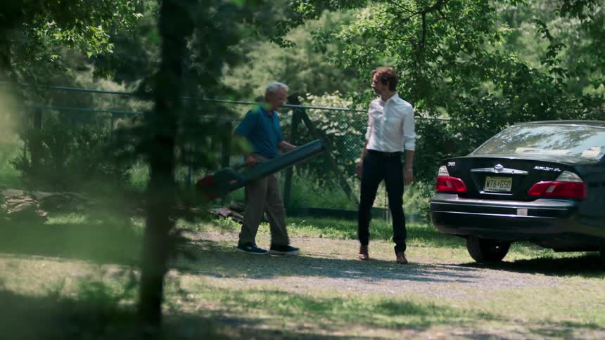A pair of men walking through a woodland carrying a large case towards a car