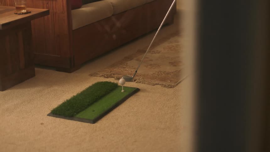 A person practice swings at a golf ball indoors